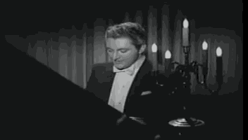 a man in a tuxedo and bow tie is playing a piano in front of a chandelier .