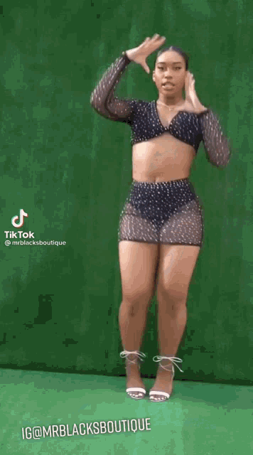 a woman in a black top and shorts is standing in front of a green background .