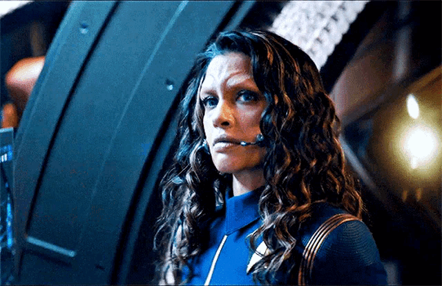 a woman with curly hair is wearing a headset while standing in a dark room .