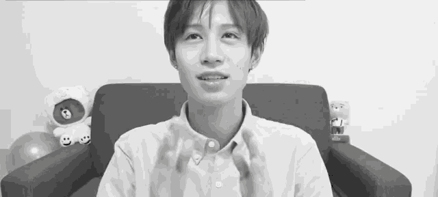 a black and white photo of a young man sitting on a couch with a stuffed animal in the background