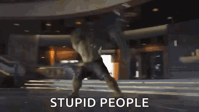 the hulk is standing in front of a building with the words stupid people written below him .