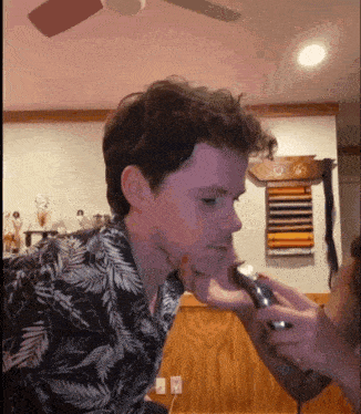 a man in a floral shirt is being shaved by a woman