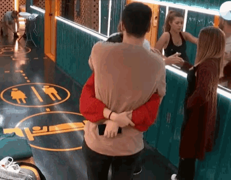 a man is hugging a woman in a hallway with a sign on the floor that says toilets