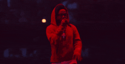a man in a hooded sweatshirt is singing into a microphone in the dark