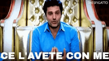a man in a blue shirt sits in a chair with the words " ce l' avete con me " written below him