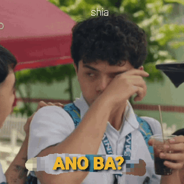 a man wipes his eyes with a straw while holding a cup of soda and a sign that says ano ba