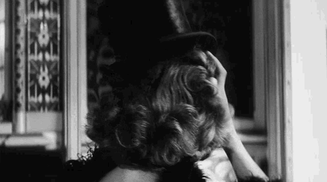 a woman in a top hat is looking at herself in the mirror .