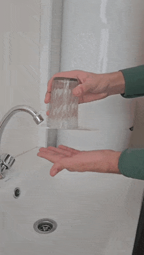 a person washing a glass in a bathroom sink