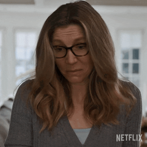 a woman wearing glasses and a grey sweater has a netflix logo on the bottom right