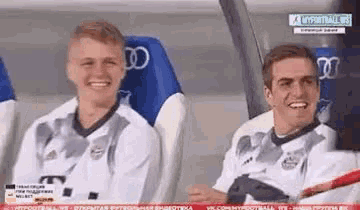 two soccer players are sitting in the dugout laughing .