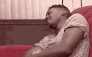 a man is laying on a red couch with his head on his arms and his eyes closed .