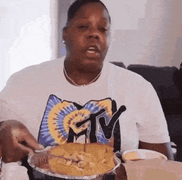 a woman wearing a tie dye shirt is eating nachos from a tin foil pan .