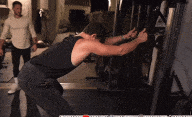 a man in a black tank top is using a machine in a gym with a youtube logo in the corner