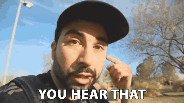 a man with a beard is pointing to his ear and says " you hear that "