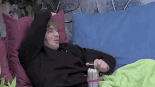 a man is laying on a bed with his arms outstretched and a can of soda .