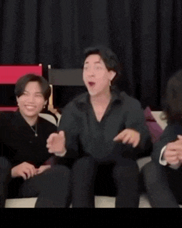 two men are sitting on a couch laughing and one of them is kicking the other 's foot .
