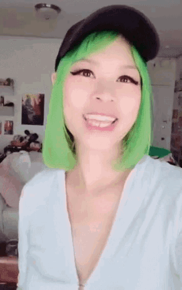a woman with green hair wearing a white shirt and a black hat