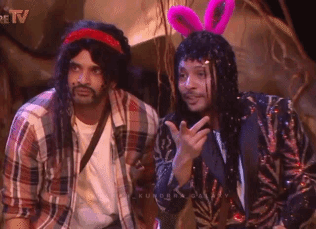 two men wearing wigs and bunny ears are standing next to each other on a stage