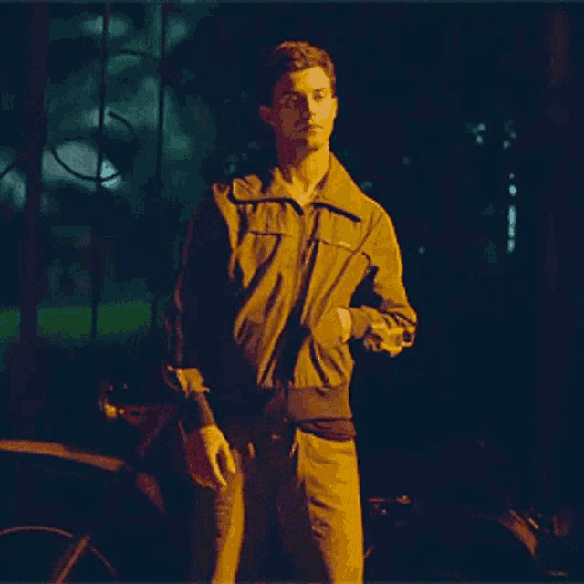 a man in a green jacket is standing in a dark room holding something in his hand .