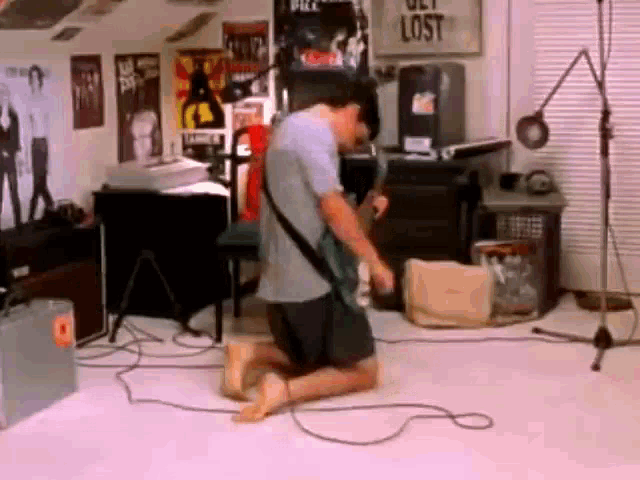 a man is kneeling on the floor playing a guitar .