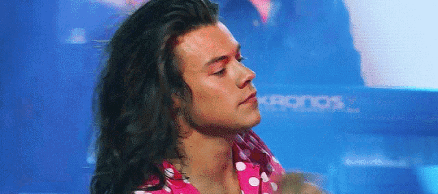 harry styles is wearing a pink and white polka dot shirt and looking at the camera .