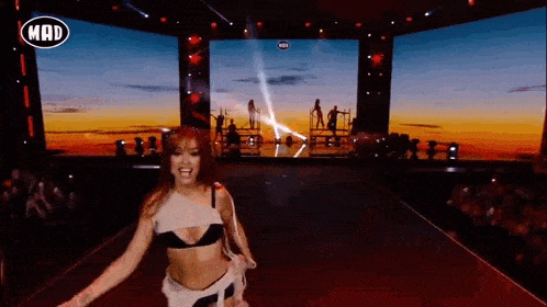 a woman is dancing on a stage in front of a large screen with the word mad on it .