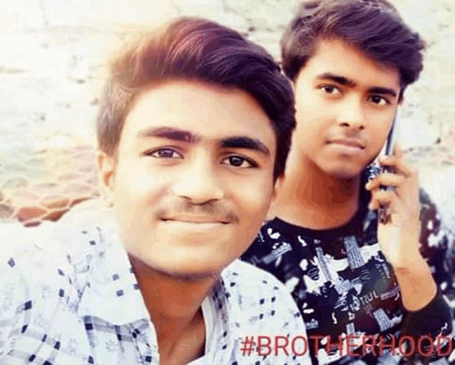 two young men are posing for a picture together . one of the men is talking on a cell phone .