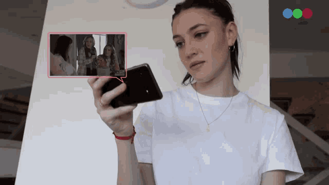 a woman in a white shirt is holding a cell phone in her right hand