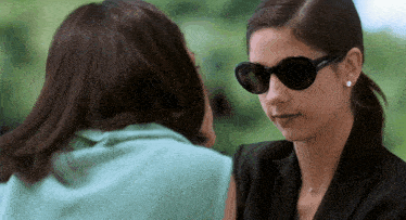 a woman wearing sunglasses looks at another woman with her hand on her forehead