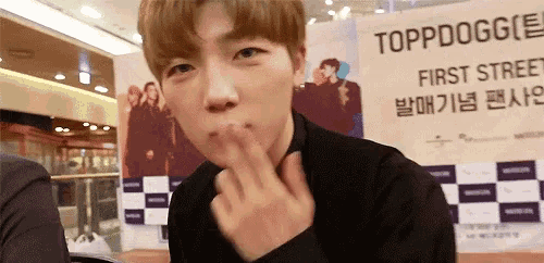 a young man is blowing a kiss in front of a sign that says toppdoggie first street