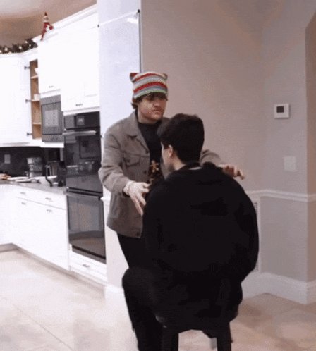 a man wearing a knitted hat is standing next to another man in a kitchen