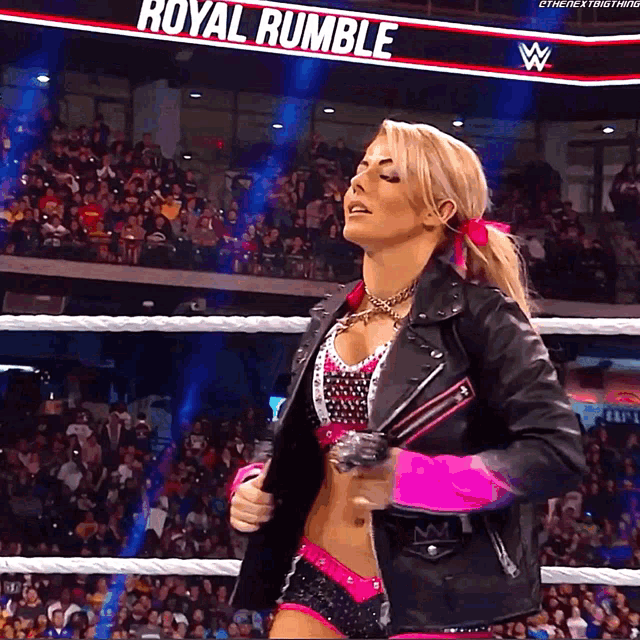 a woman in a leather jacket stands in front of a sign that says royal rumble on it