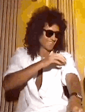 a man wearing sunglasses and a white shirt is smiling and holding a glass .