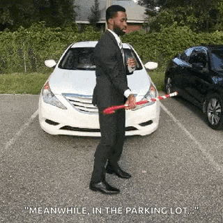 a man in a suit is standing in front of a white car holding a bat .