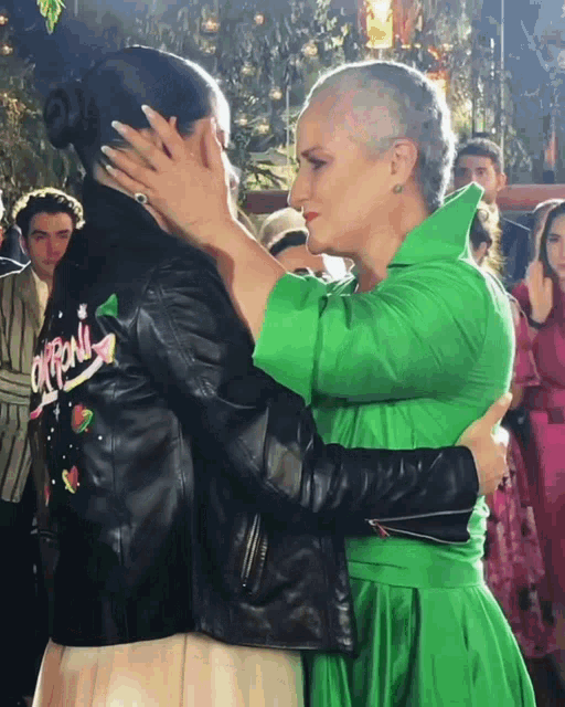 a woman in a green dress hugging another woman in a black jacket