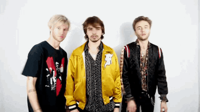 three young men are standing next to each other and one of them is wearing a yellow jacket with the letter f on it .
