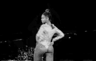 a woman in a white bodysuit is dancing on a stage in a black and white photo .