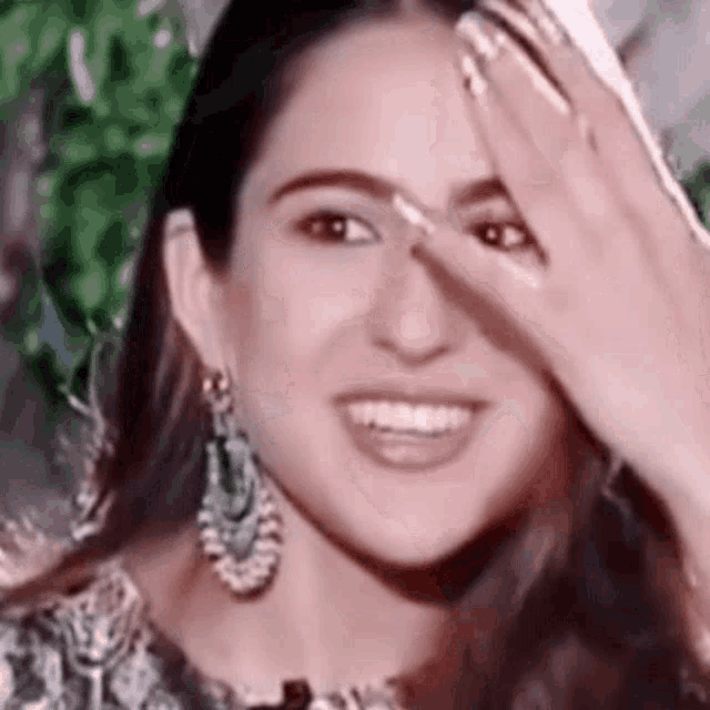 the woman is smiling and covering her face with her hand .