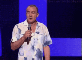 a man in a hawaiian shirt is holding a microphone and speaking into it