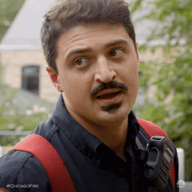 a man with a mustache and beard is wearing a black shirt and a red strap .