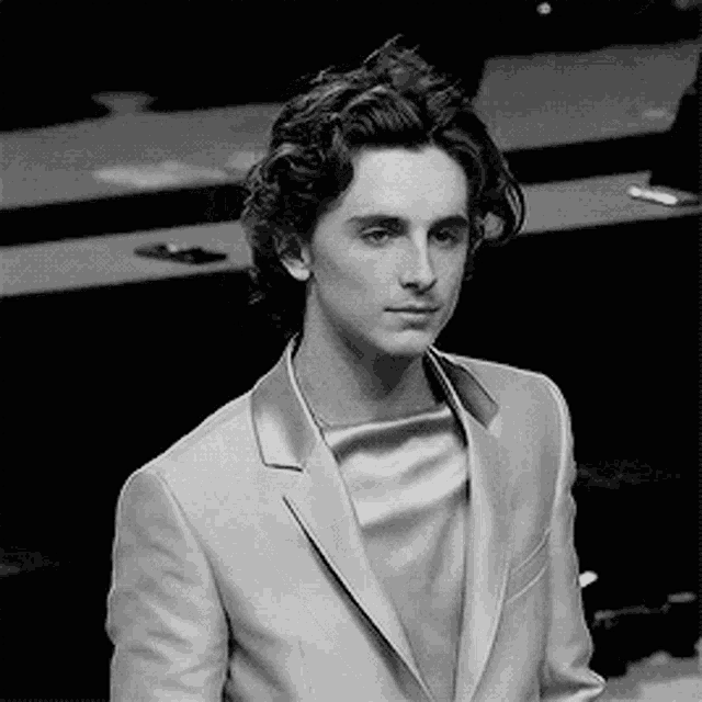 a black and white photo of a young man wearing a suit and looking at the camera .