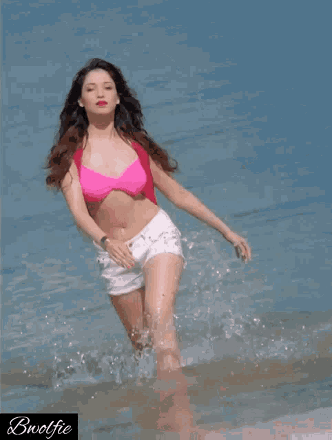 a woman in a pink bikini and white shorts is standing in the water