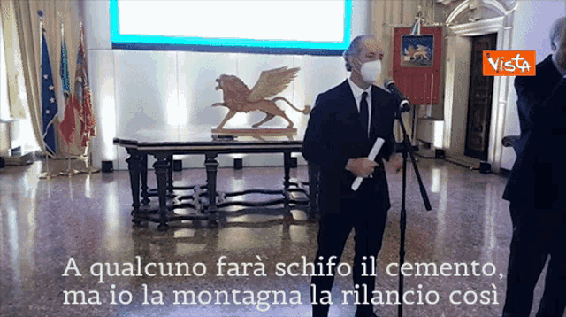 a man wearing a mask stands in front of a microphone with vista written on the bottom of the screen