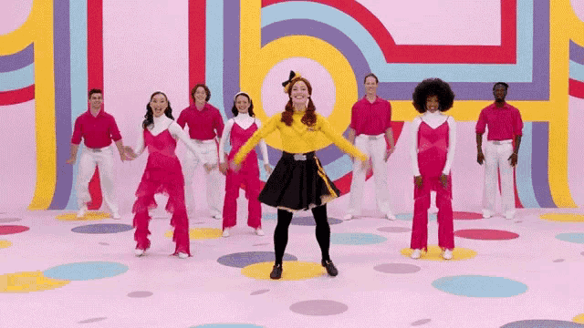 a group of people are dancing in front of a colorful wall with the letter h on it