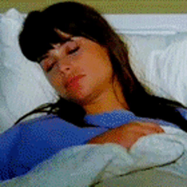 a woman in a blue shirt is laying in a hospital bed with her eyes closed