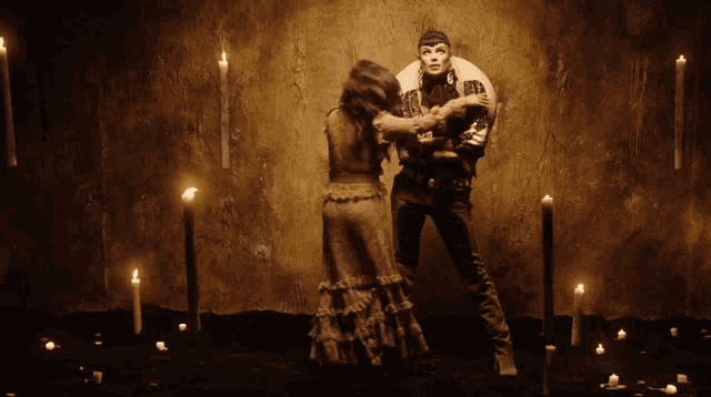 a man and woman are dancing in a dark room with candles