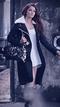 a woman in a white dress and a black coat holds a black purse