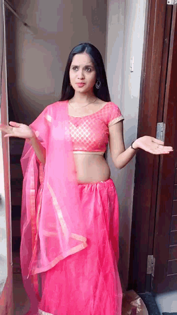 a woman in a pink dress is standing in front of a door with her arms outstretched