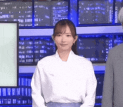 a woman in a white shirt is standing in front of a man in a suit in a newsroom .