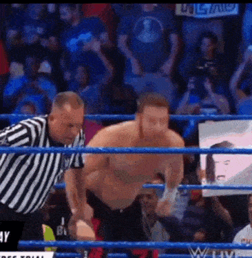 a referee is standing next to a wrestler in a wrestling ring with a crowd watching .